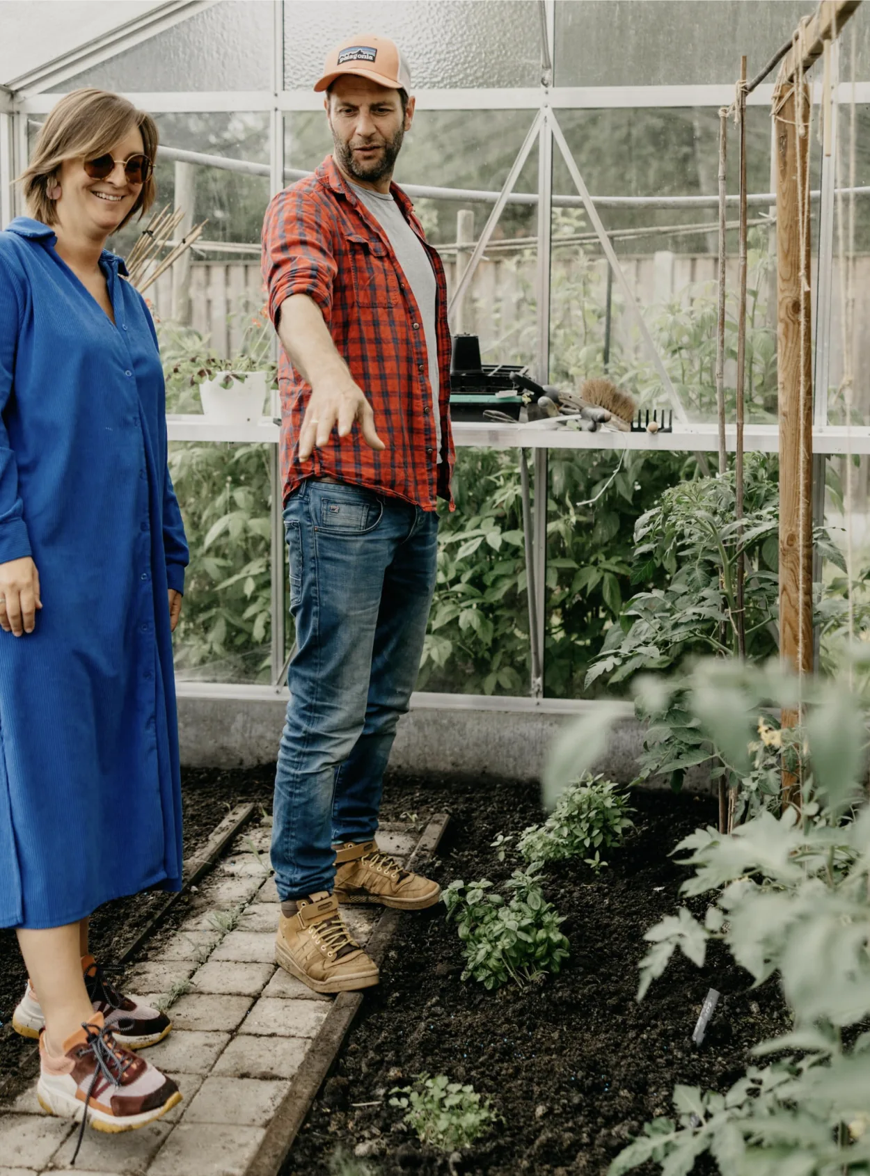 Tuinontwerpers van Studio Buiten in gesprek in een serre met moestuin en tomatenplanten